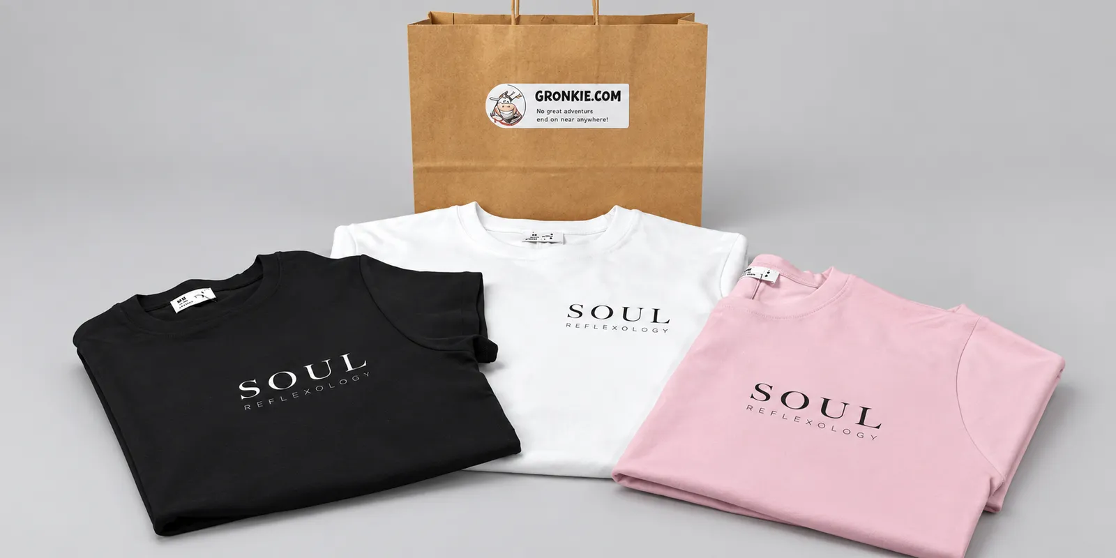 three folded tees printed with a small business logo, next to a Gronkie bag